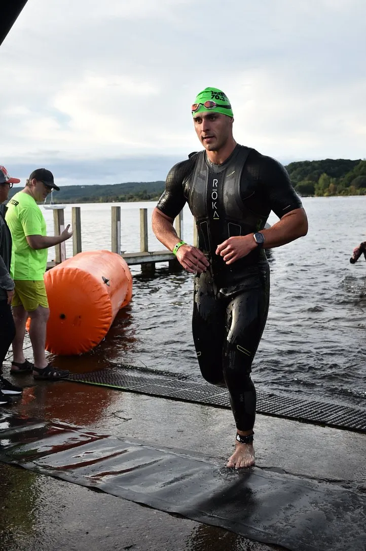 James running out of the lake after the swim in a wetsuit and green cap